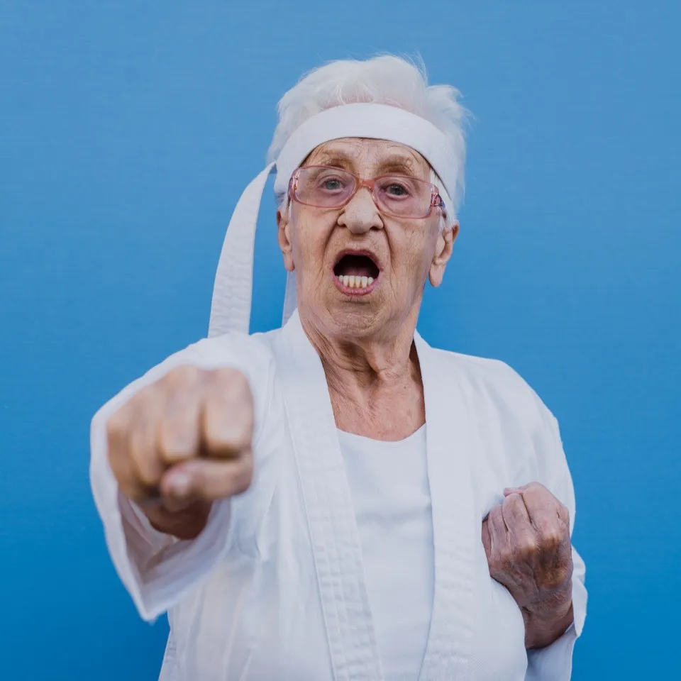 An energetic older woman in a karate outfit throwing a punch